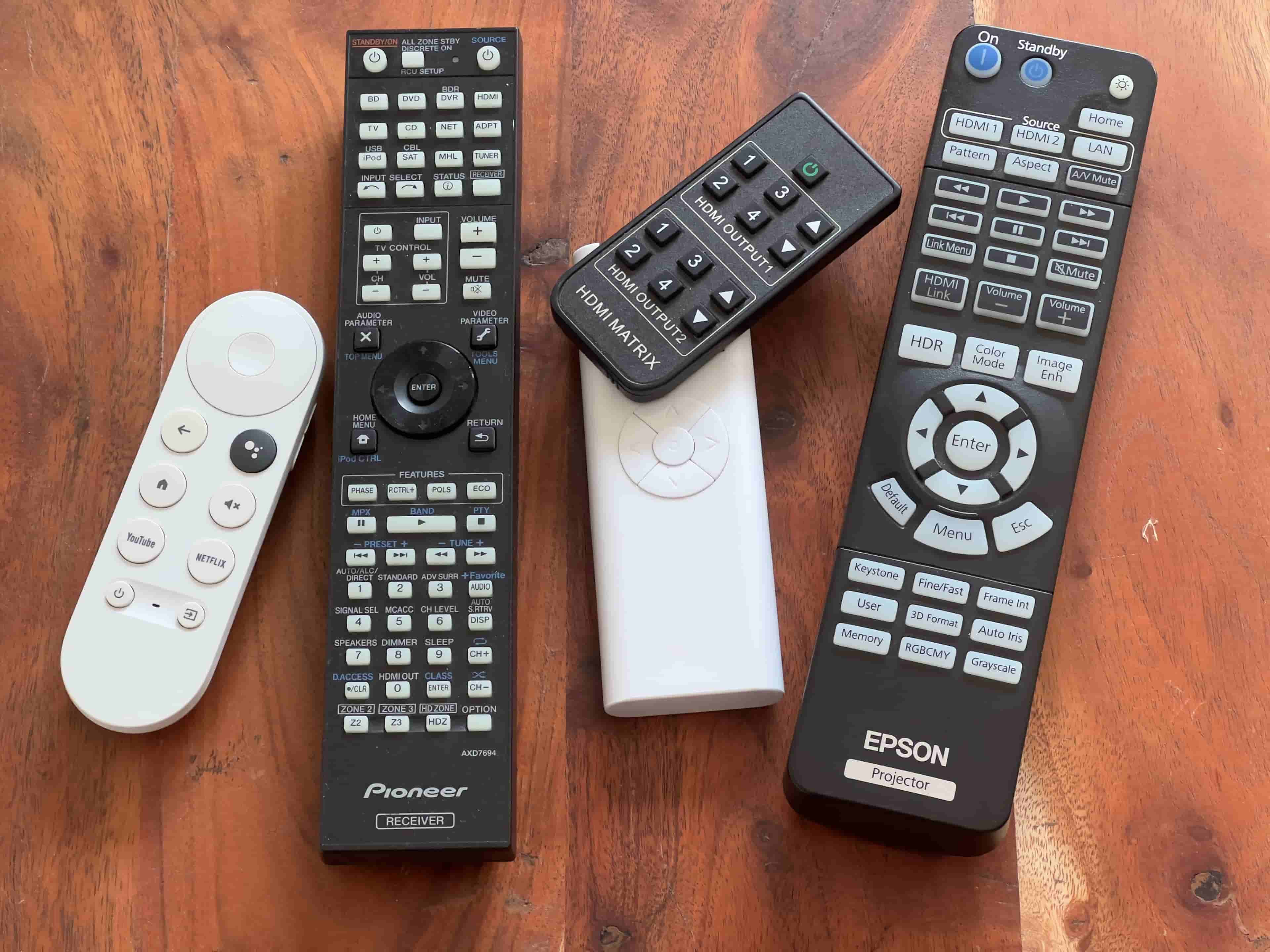 A picture several remote control units on a wooden table.